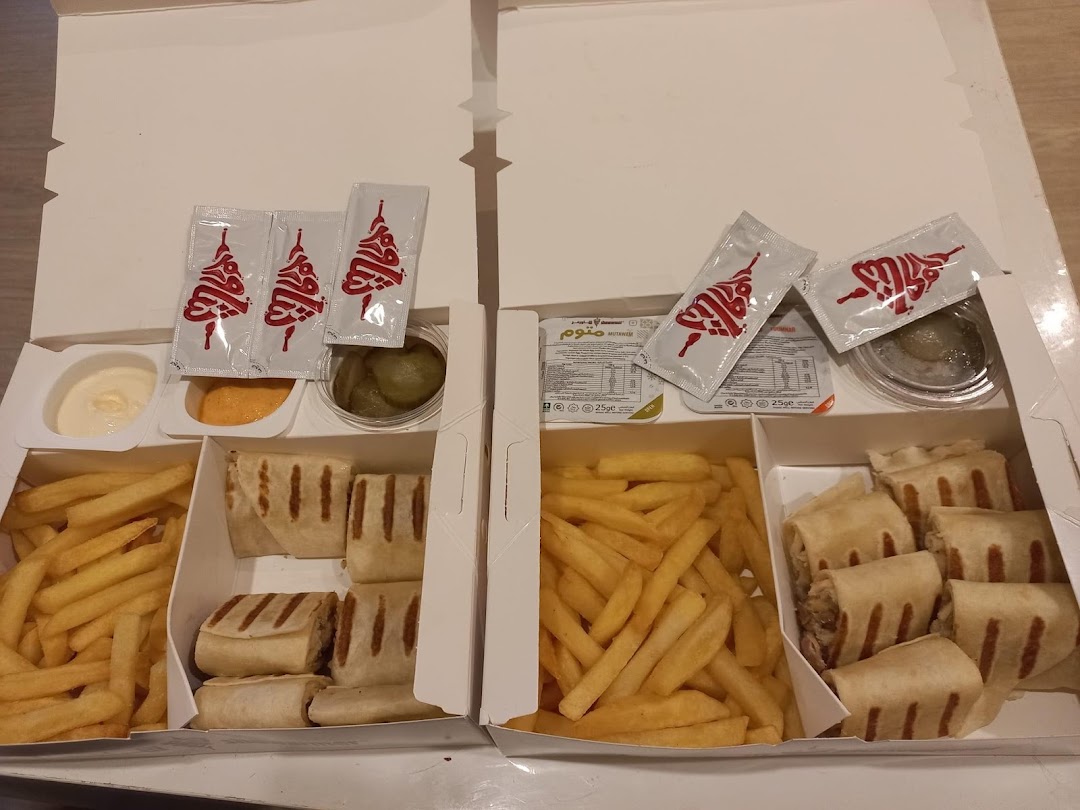 Two takeaway boxes filled with shawarma wraps, french fries, pickles, and dipping sauces.