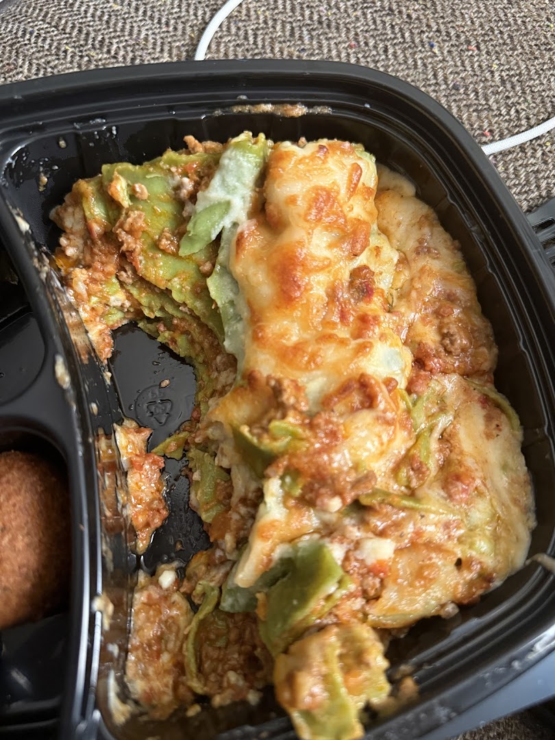 A close-up of a delicious-looking lasagna dish in a black takeout container.