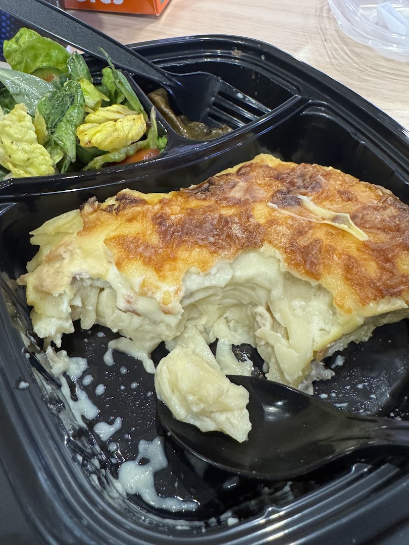 A close-up of a creamy, layered dish with a side salad in a black takeout container.