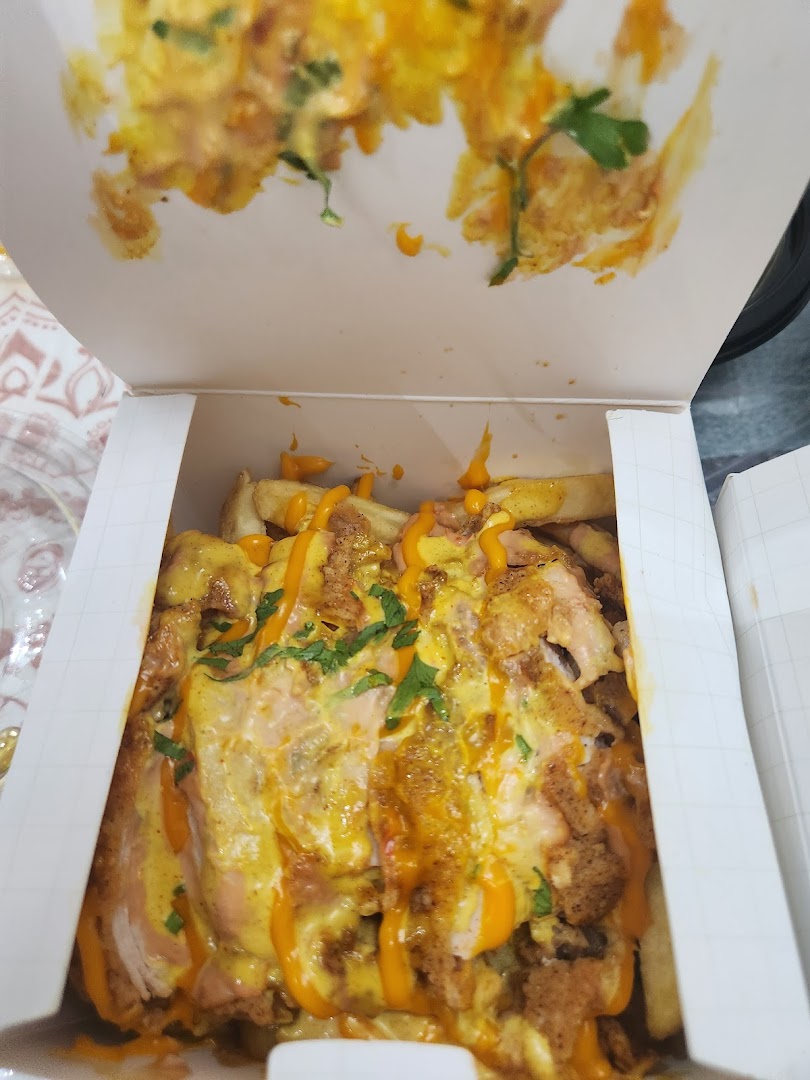 A close-up shot of loaded fries with cheese sauce and meat toppings in a white takeout box.
