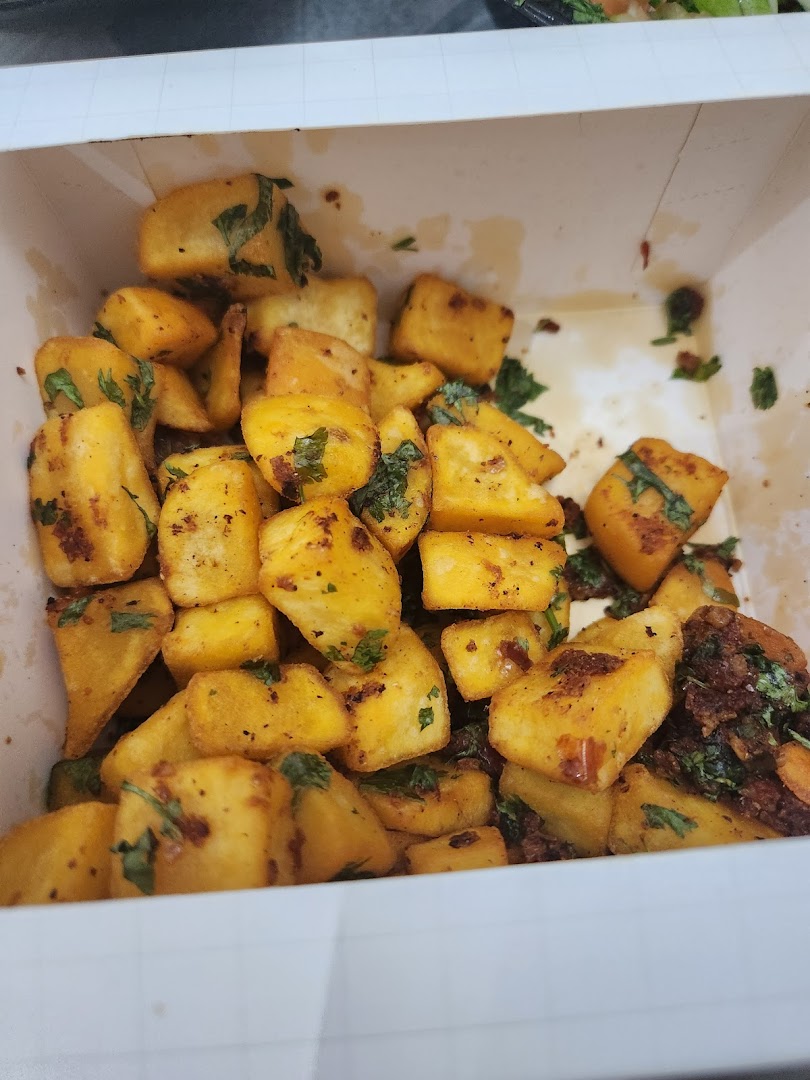 A close-up of crispy fried potato cubes seasoned with herbs and spices in a white container.