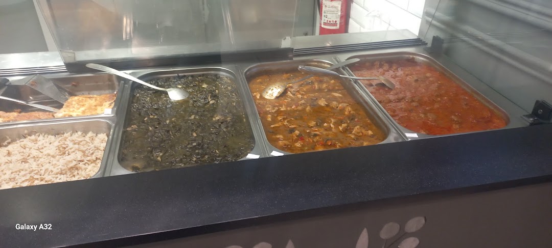 A display of various prepared dishes in metal trays, including rice, greens, and stews.
