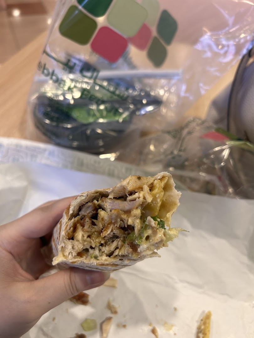 A hand holds a delicious-looking shawarma wrap, with a branded bag in the background.