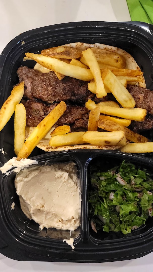 A takeout container filled with grilled meat, french fries, hummus, and a side salad.