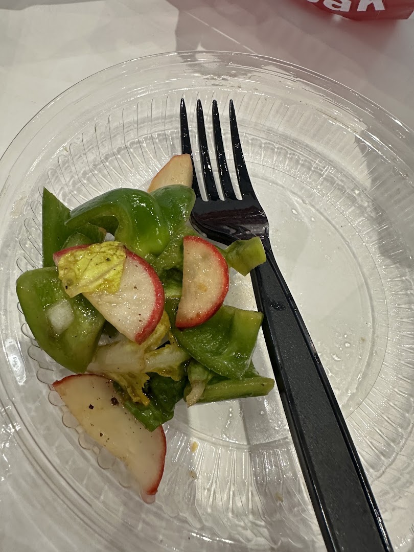 A close-up of a salad with green peppers and apple slices on a clear plastic plate with a fork.