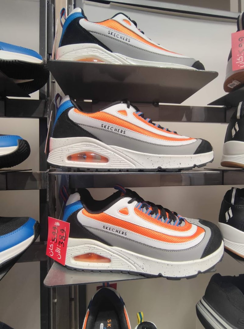 Skechers shoes displayed on shelves, featuring orange and white designs with visible price tags.