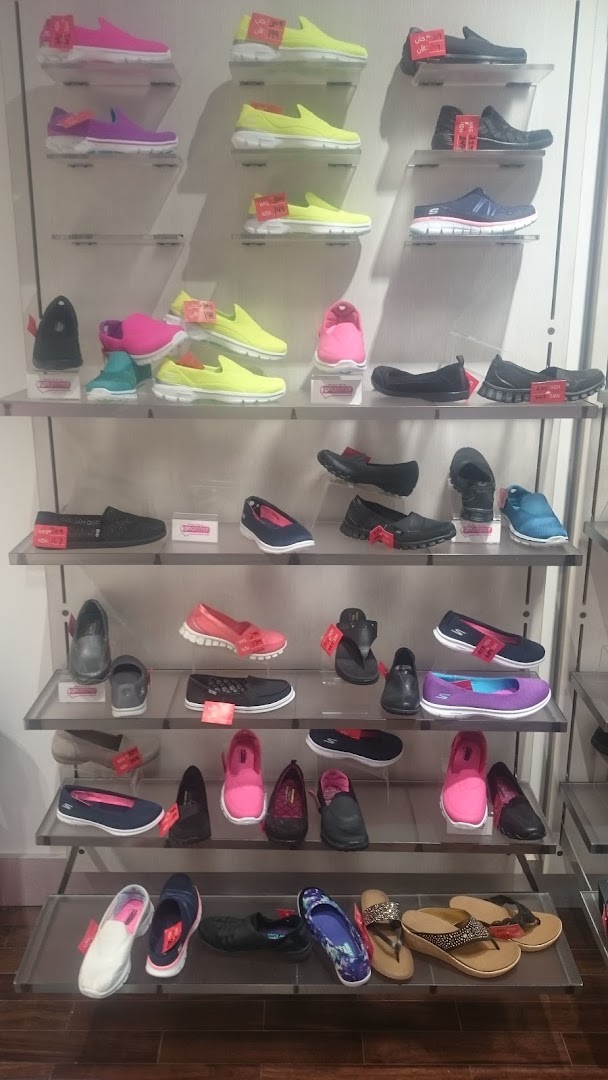 A display of various Skechers shoes, including sneakers, flats, and sandals, on shelves.