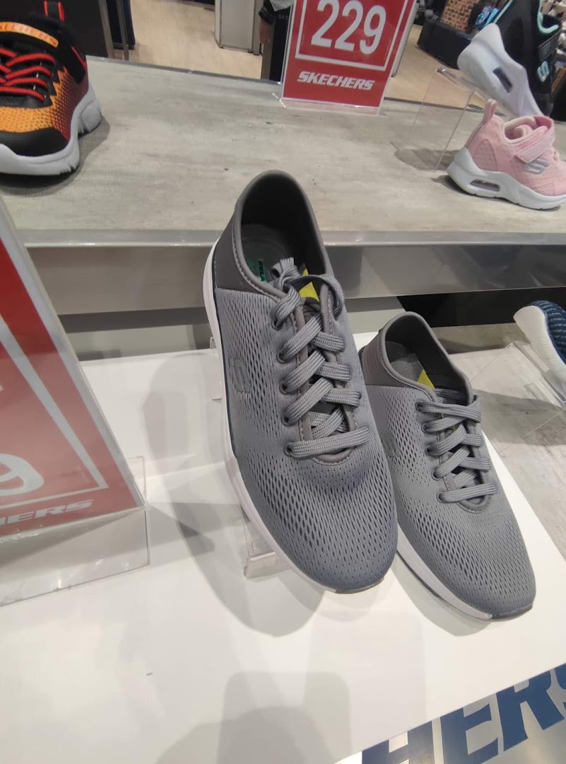 Close-up of grey Skechers sneakers displayed on a white shelf with other shoes in the background.