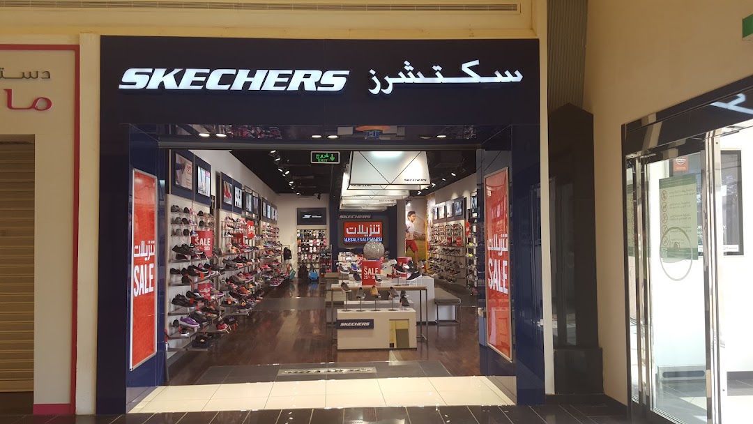 The entrance of a Skechers shoe store with displays of shoes and sale signs.