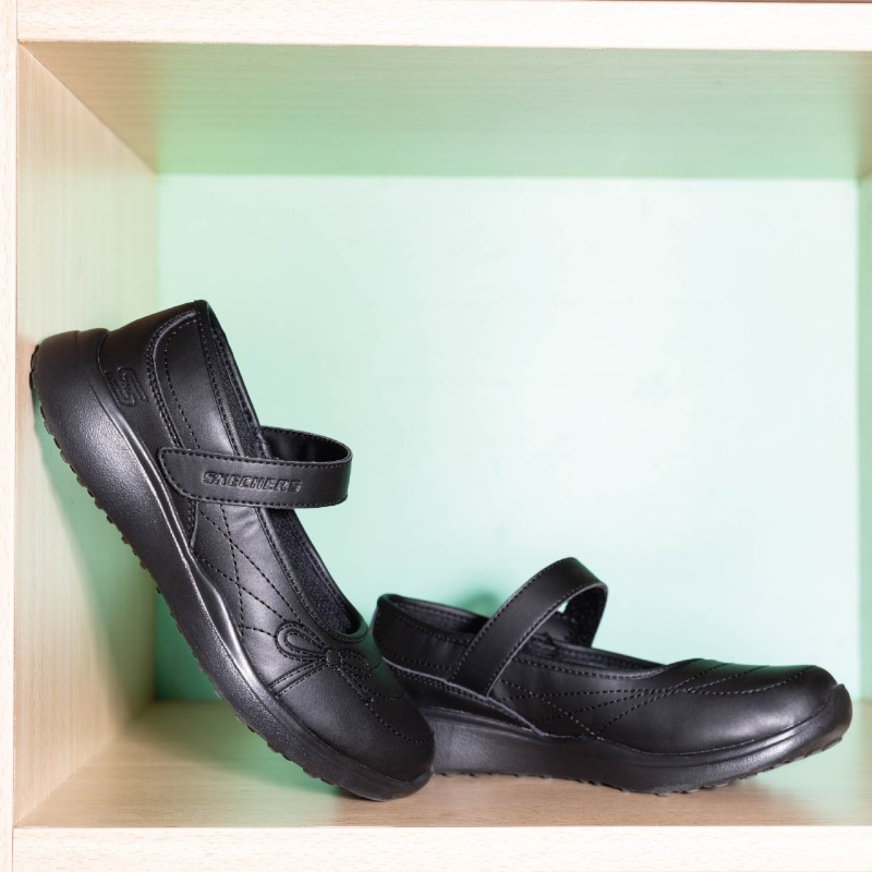 A pair of black Skechers Mary Jane shoes with velcro straps displayed on a shelf.