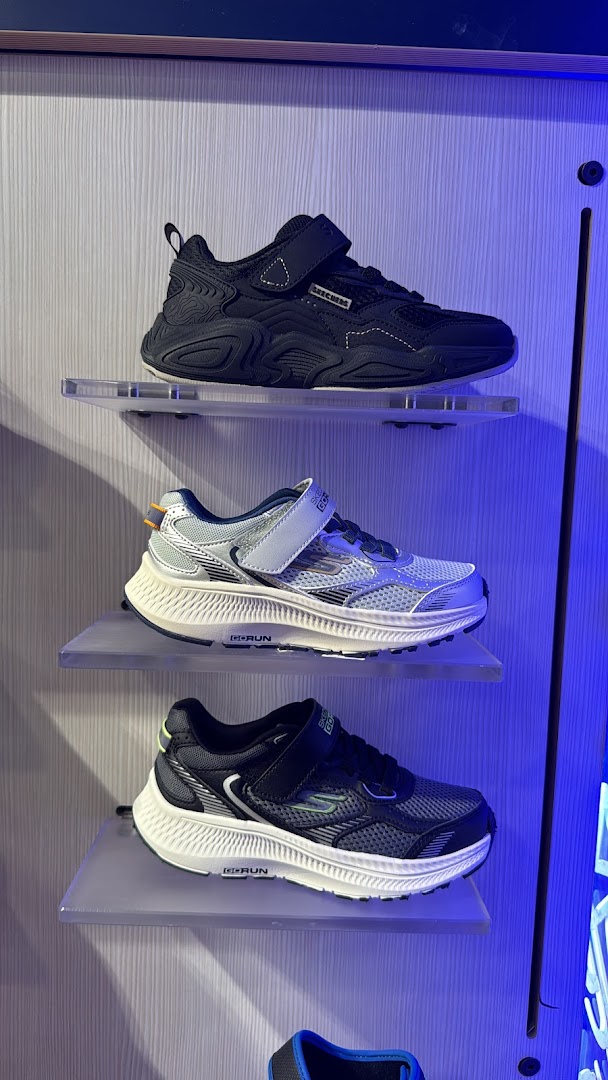 Three pairs of Skechers children's shoes displayed on shelves with blue lighting.