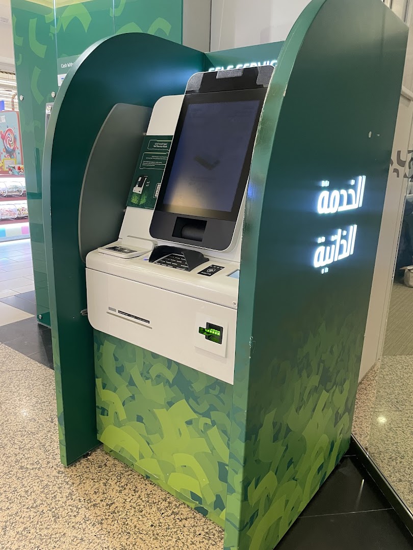 A green self-service kiosk with a touchscreen and Arabic text for SNB AlAhli.