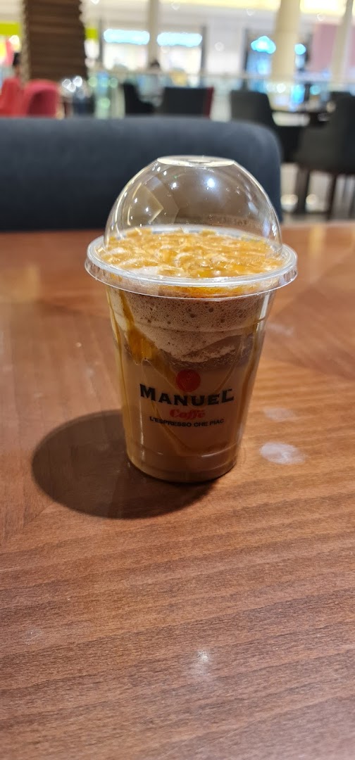 A close-up of a caramel iced coffee drink in a clear plastic cup with a dome lid.