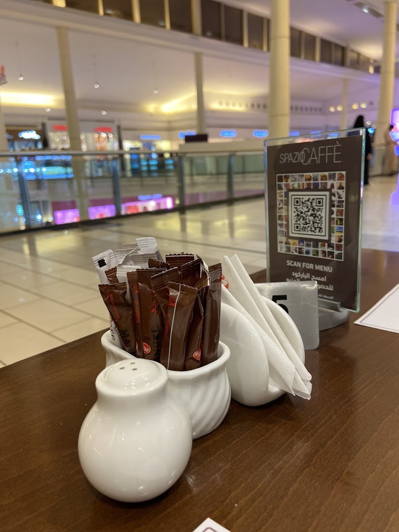 A table setting at Spazzio Caffè with sugar packets, salt shaker, and napkins, with a QR code menu in the background.