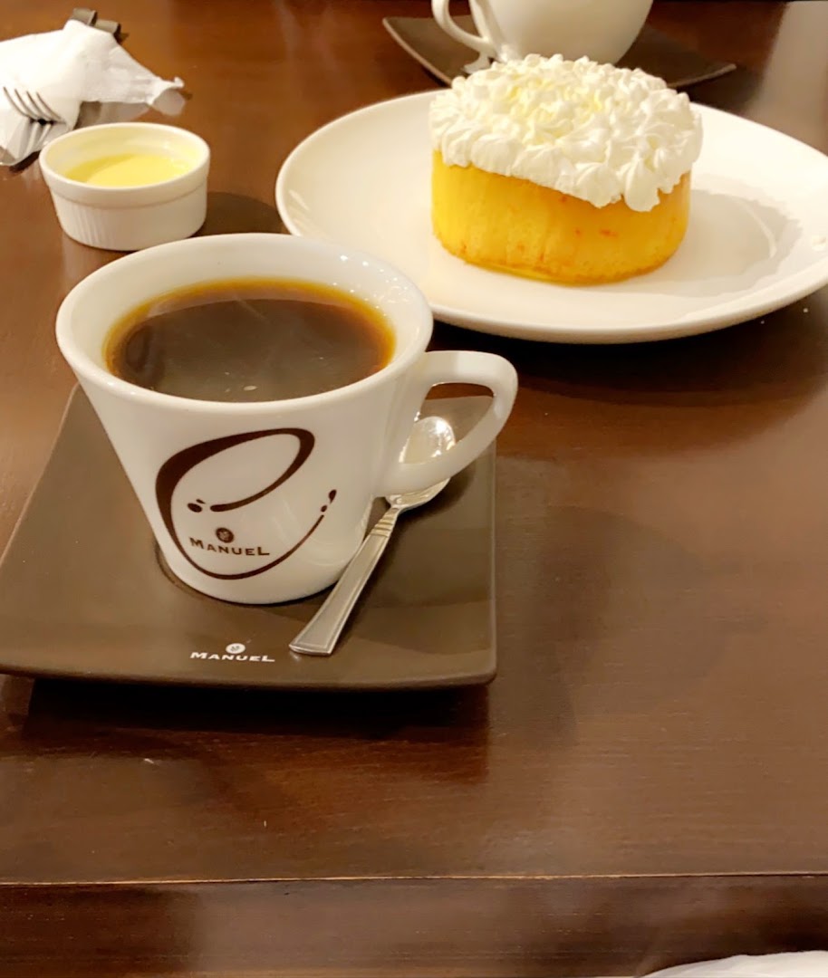 A cup of black coffee and a small cake with whipped cream on a table.