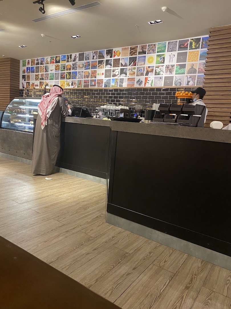A customer orders at the counter of Spazzio Cafe, with a wall decorated with various images.