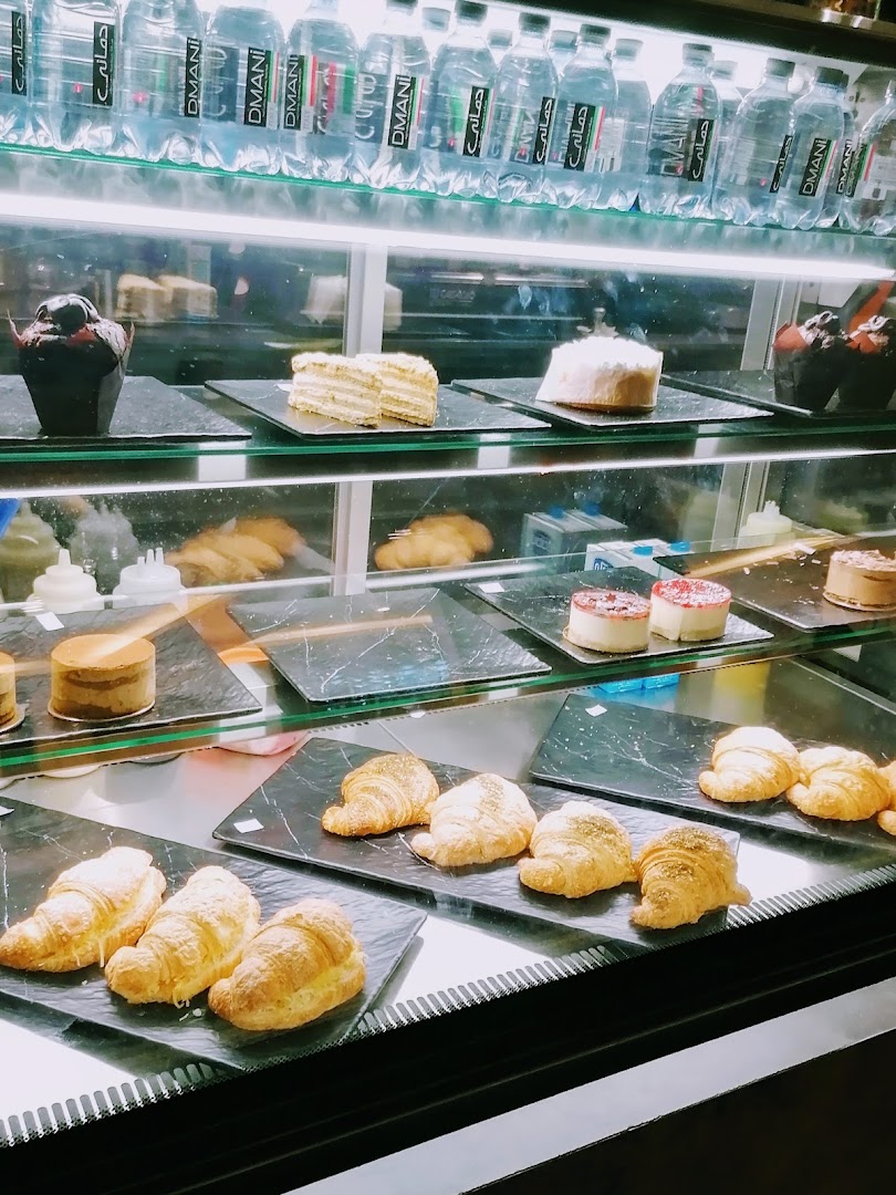A display case filled with various pastries, cakes, and bottled water.