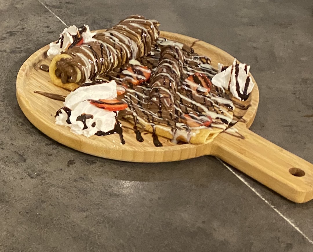 A wooden board with a waffle topped with chocolate, strawberries, and whipped cream.
