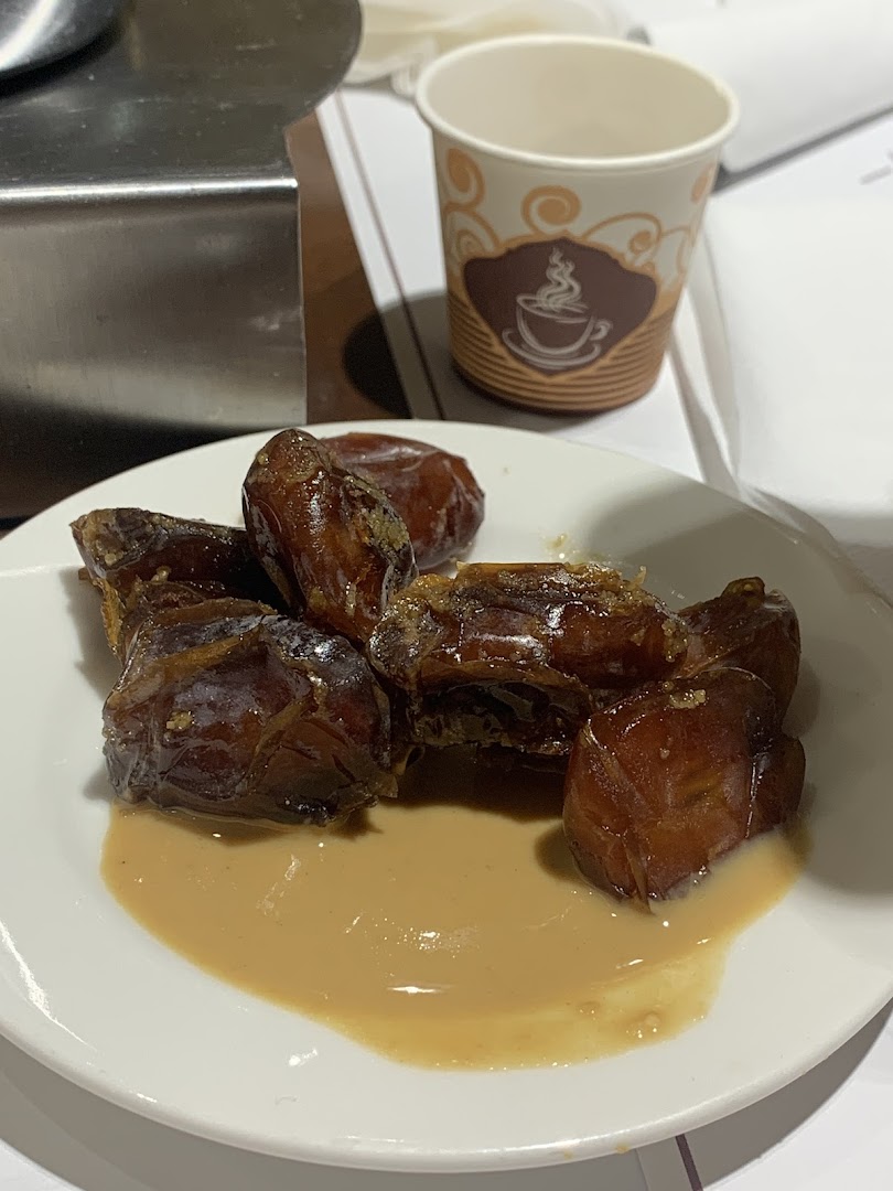 A plate of dates with a creamy sauce, next to a disposable coffee cup.