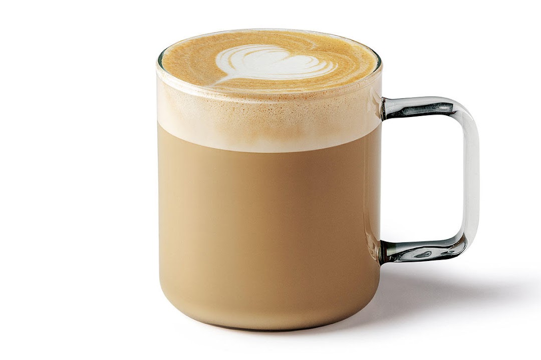 A clear glass mug filled with a latte, featuring latte art in the shape of a heart.