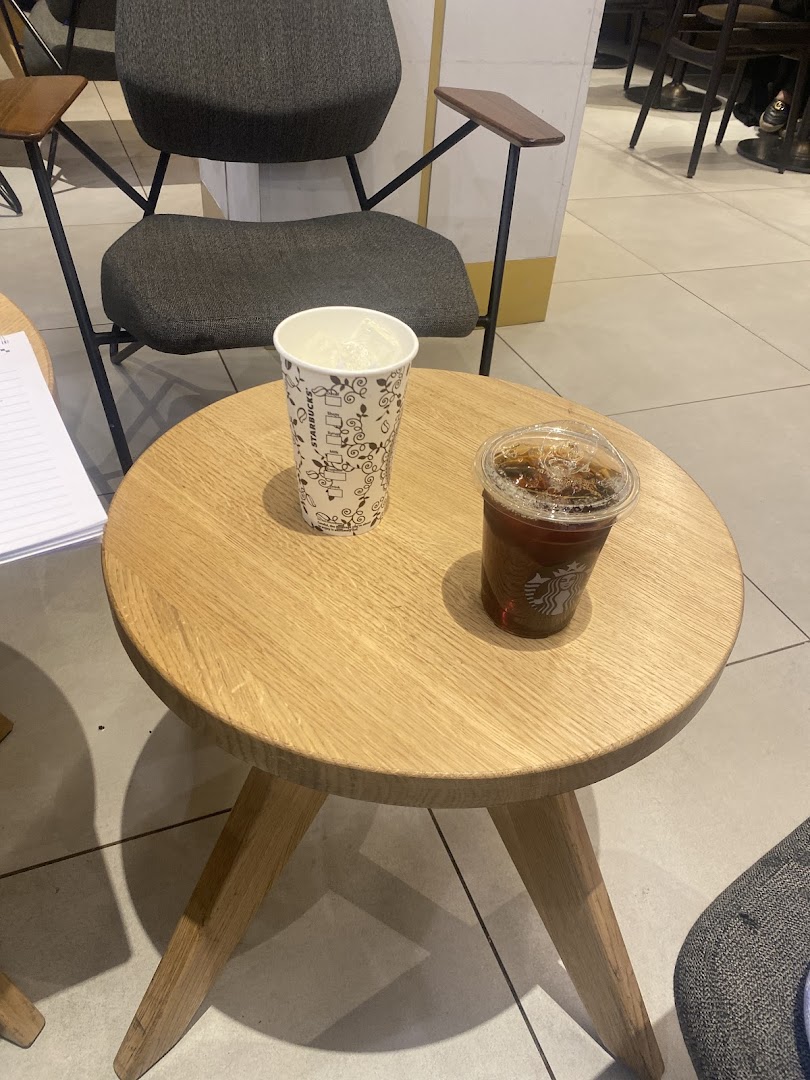 Two Starbucks drinks on a small wooden table with chairs in the background.