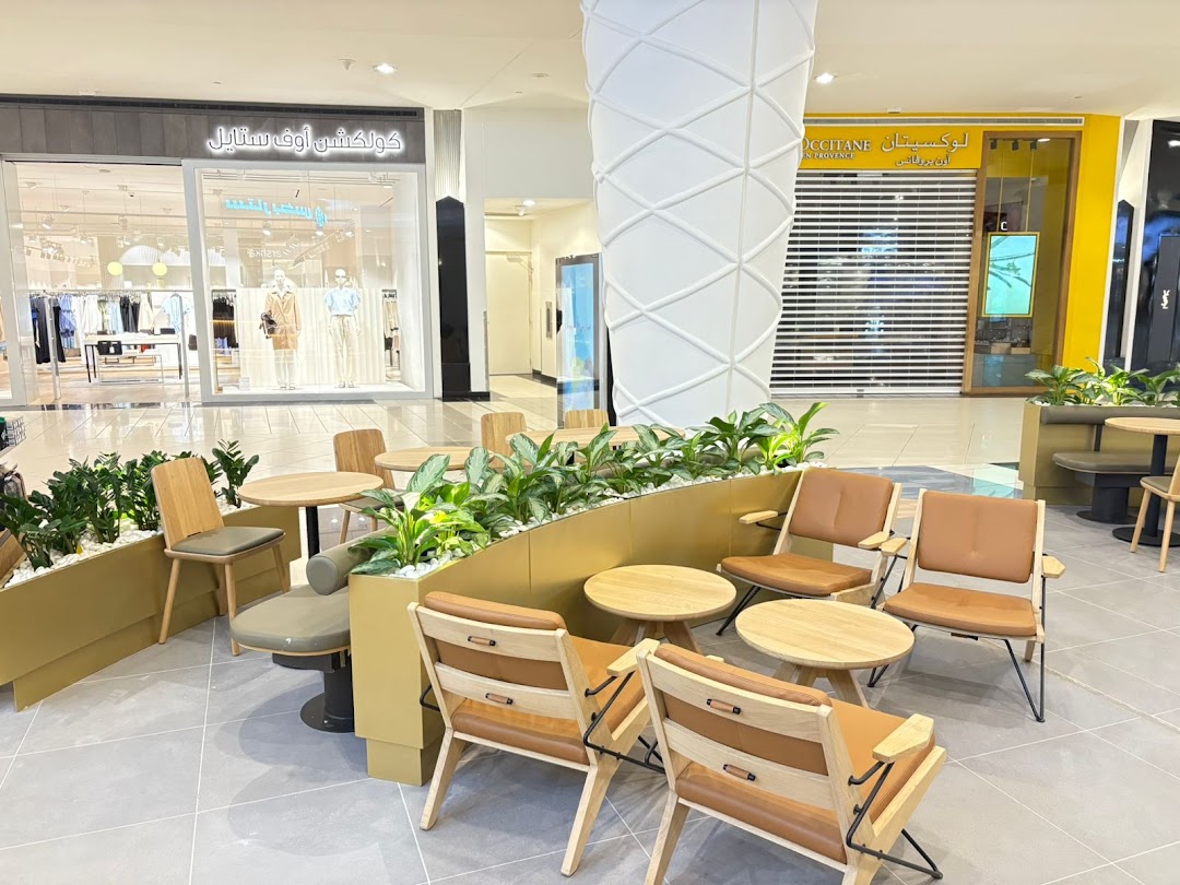A seating area with modern chairs and tables, surrounded by plants, in a shopping mall.