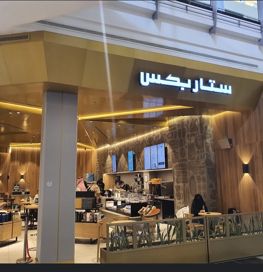 The exterior of a Starbucks coffee shop with Arabic signage and a warm, inviting interior visible.