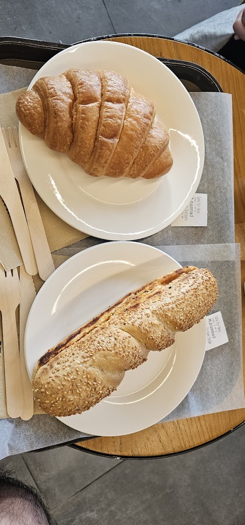 Two plates with a croissant and a sesame seed bread are on a table.