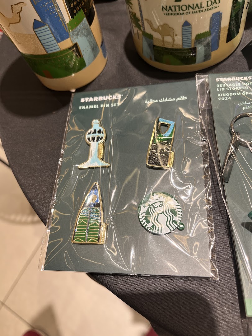 Starbucks enamel pin sets and mugs featuring Saudi Arabian landmarks and national day themes.