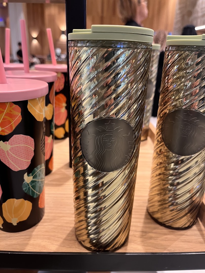 Close-up of Starbucks tumblers, one with a gold ribbed design and the other with a pumpkin pattern.