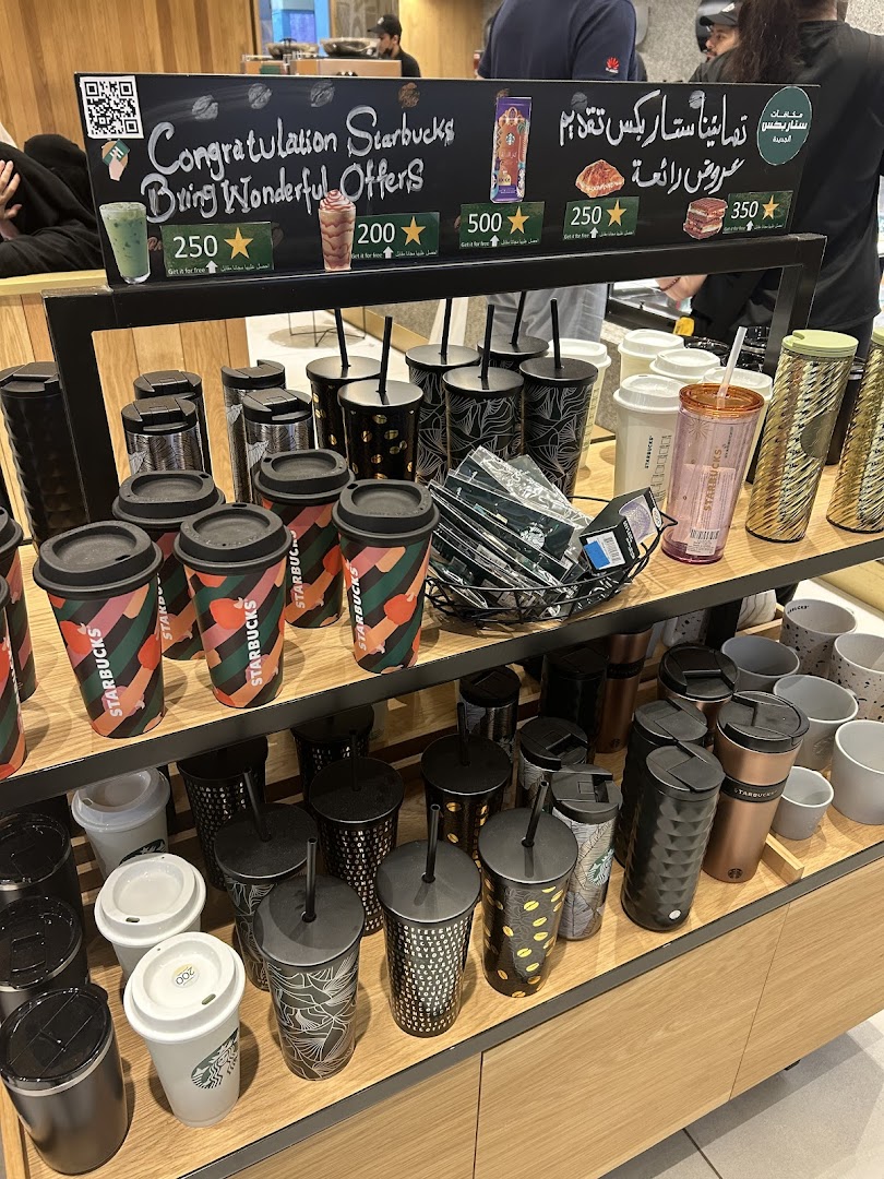 A display of Starbucks merchandise, including cups and tumblers, with a promotional sign.