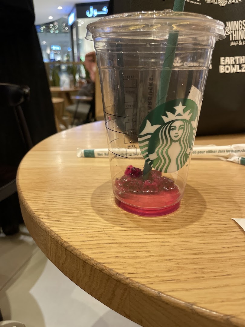 An empty Starbucks cup with a straw and remnants of a pink drink on a wooden table.