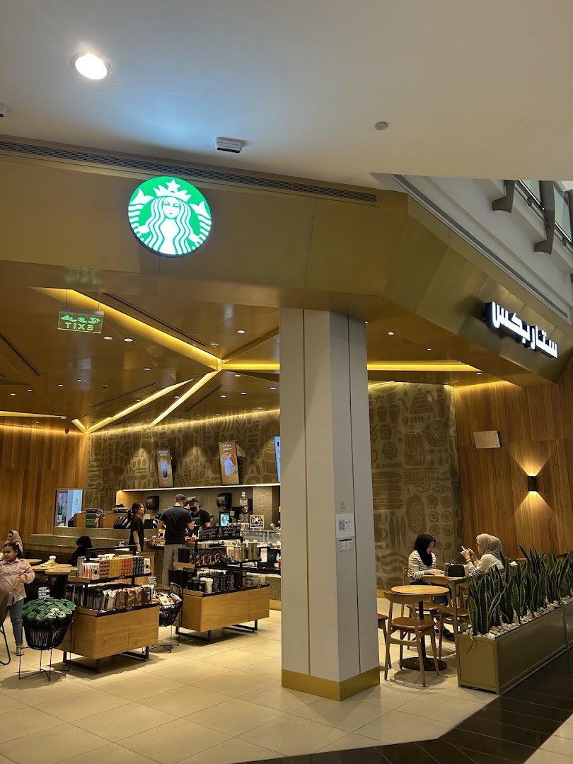 The exterior of a Starbucks coffee shop with customers inside and seated at tables.