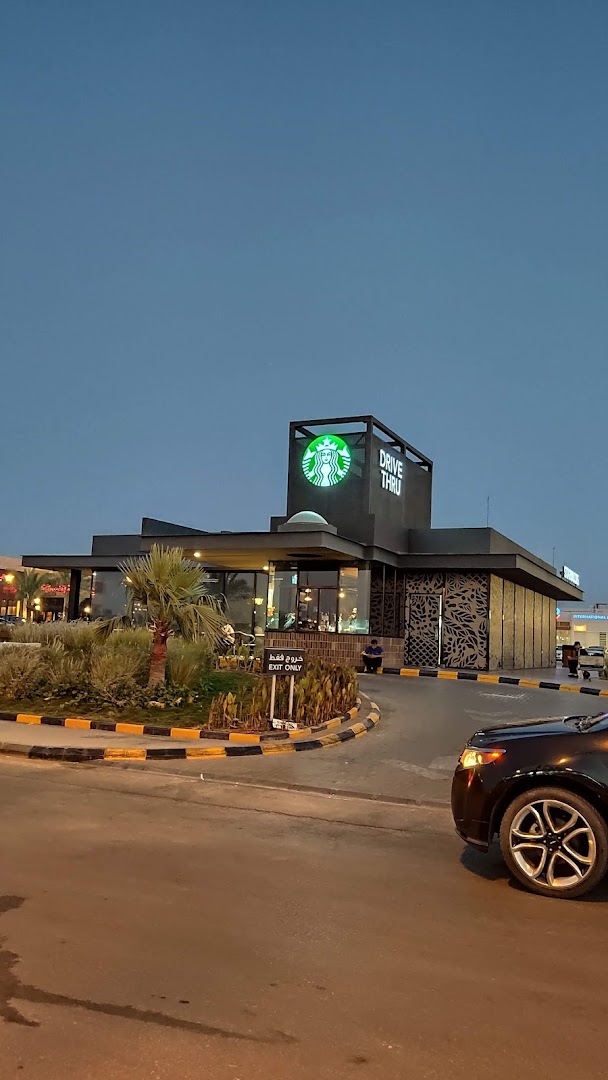 A Starbucks drive-thru location with its iconic logo illuminated against a twilight sky.