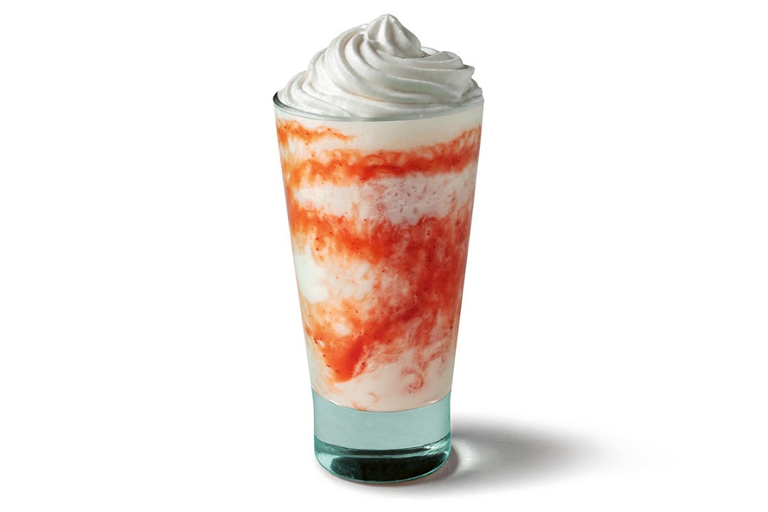 A tall glass of Starbucks strawberry frappuccino with whipped cream.