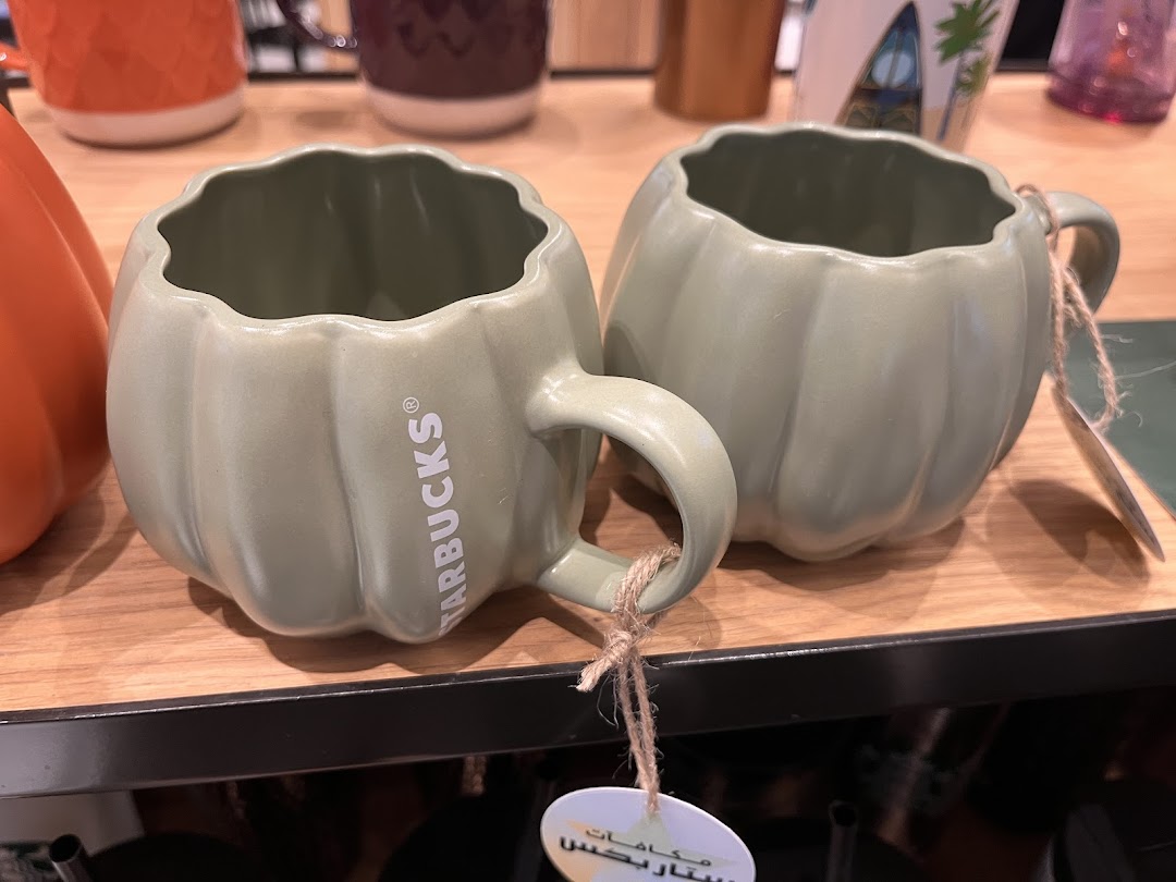 Two sage green pumpkin-shaped mugs with Starbucks branding displayed on a wooden shelf.