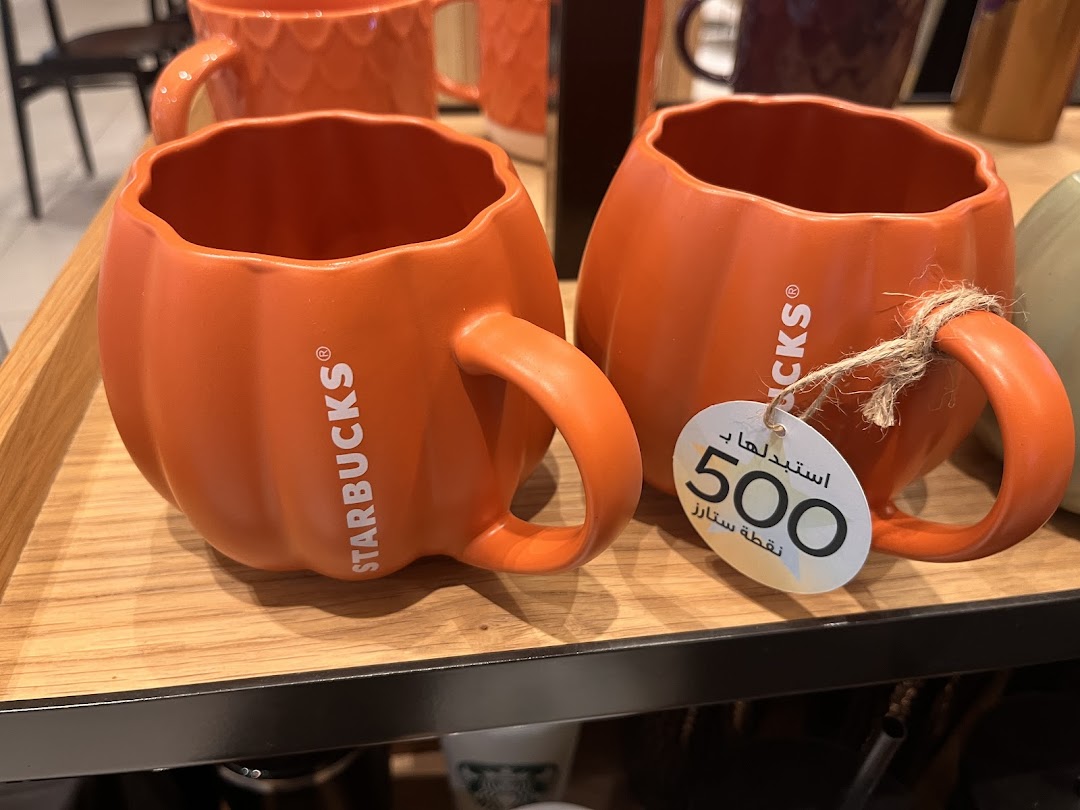 Two orange pumpkin-shaped mugs with Starbucks branding displayed on a wooden shelf.