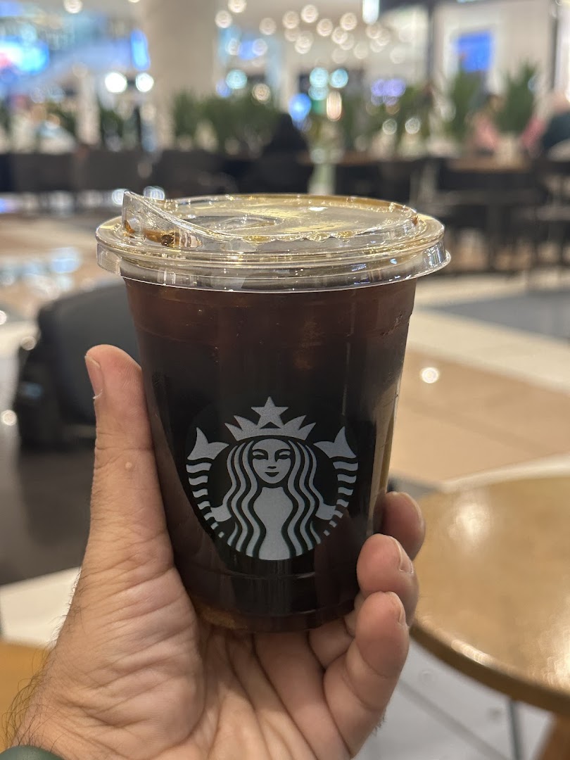 A hand holds a Starbucks iced coffee cup with the iconic logo.