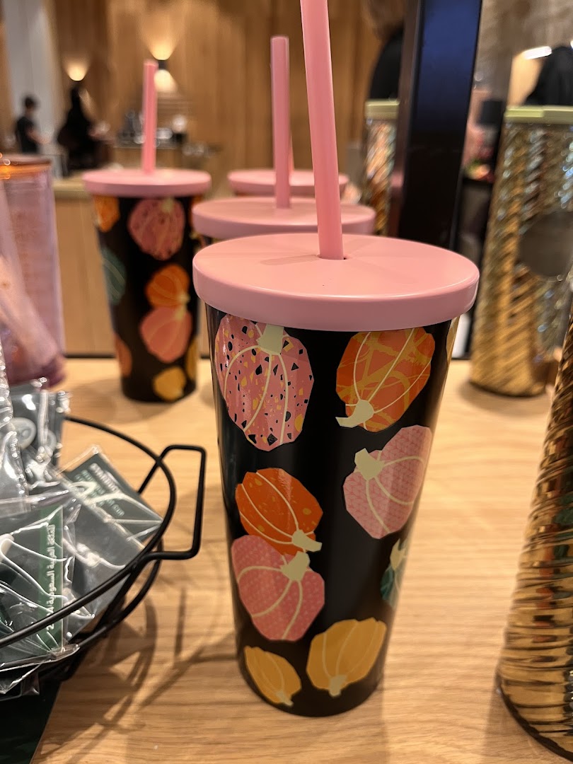 A close-up of Starbucks tumblers with a festive pumpkin design and pink lids.