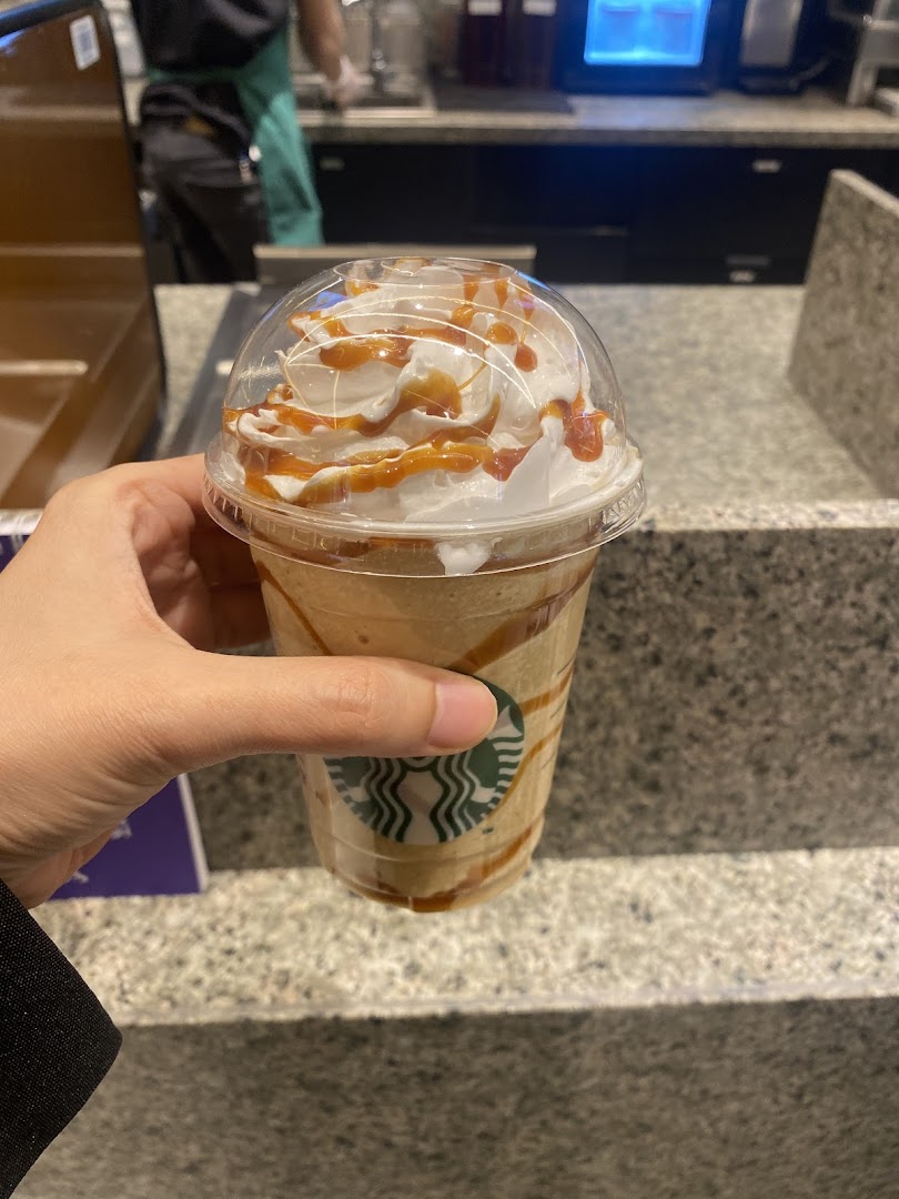 A hand holds a Starbucks drink topped with whipped cream and caramel drizzle.