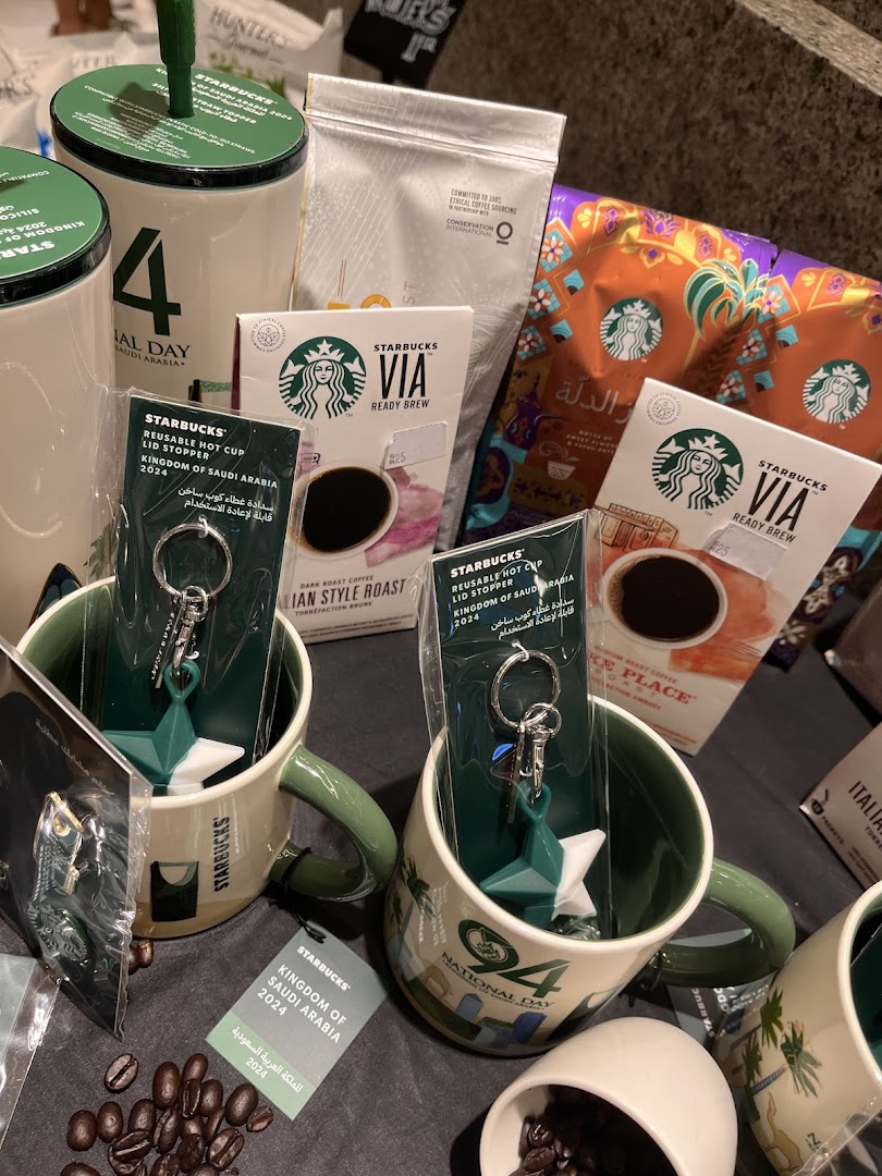 Starbucks merchandise including mugs, coffee, and keychains with Saudi National Day theme.