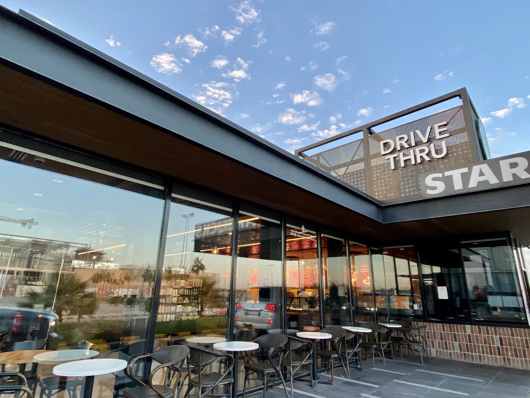 Exterior view of a Starbucks with a drive-thru sign and outdoor seating.