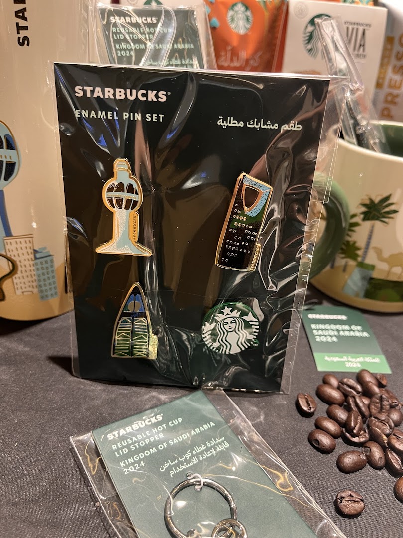 Starbucks merchandise including an enamel pin set, reusable hot cup lid stopper, and coffee beans.