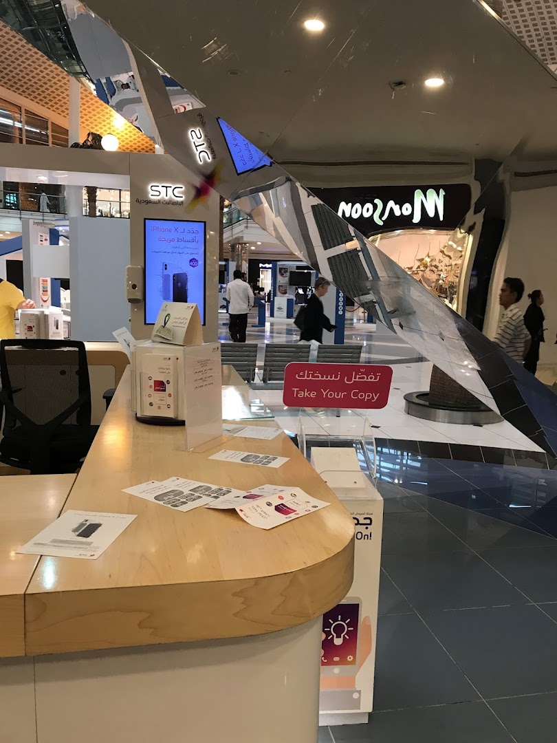 A retail store counter with promotional materials and a digital display showing an iPhone.