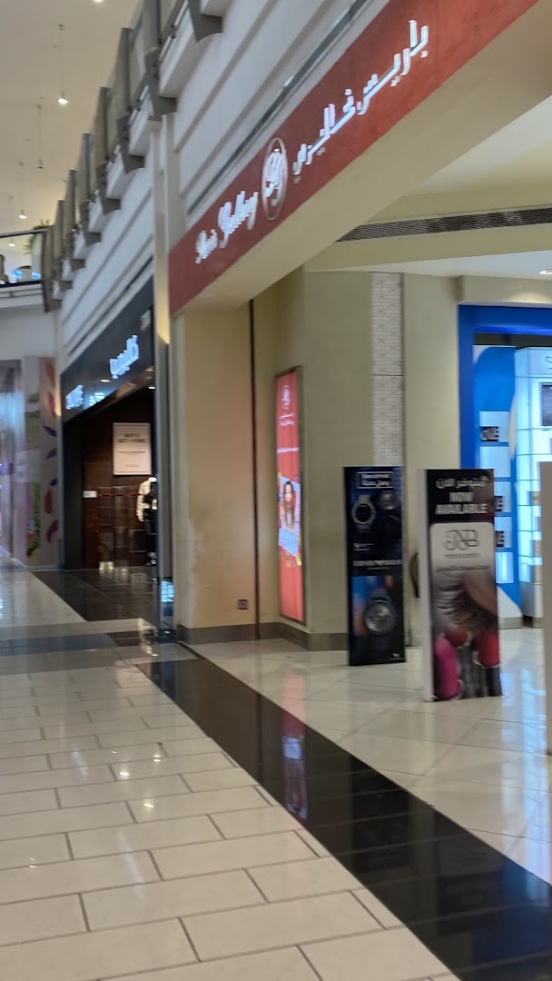 A shopping mall corridor with various store entrances and promotional displays.