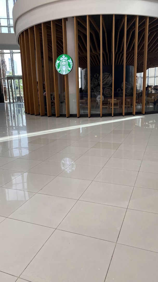 The iconic Starbucks logo is displayed on a modern, wooden-slatted structure inside a bright, spacious mall.