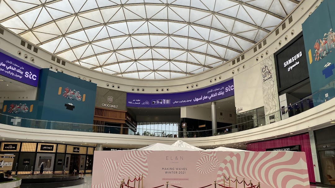 A wide shot of a shopping mall interior with various stores and a large atrium ceiling.