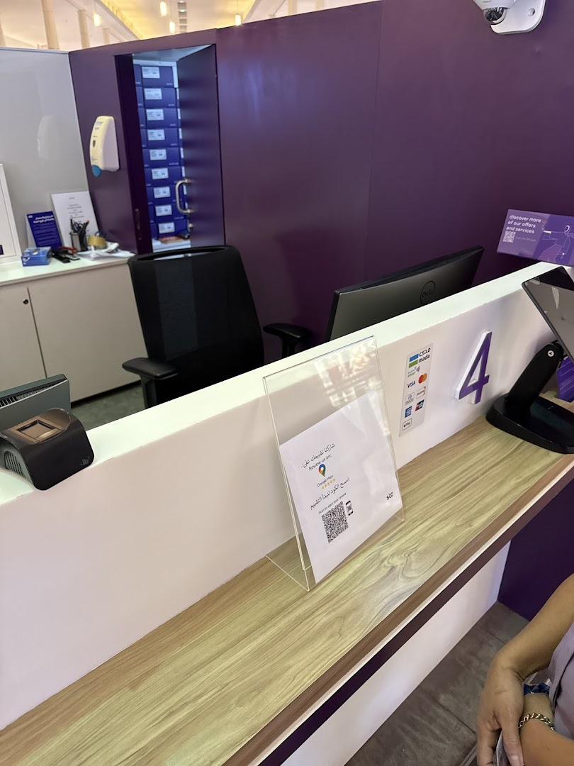 Interior view of a stc store counter with a computer, payment terminal, and a sign with a QR code.