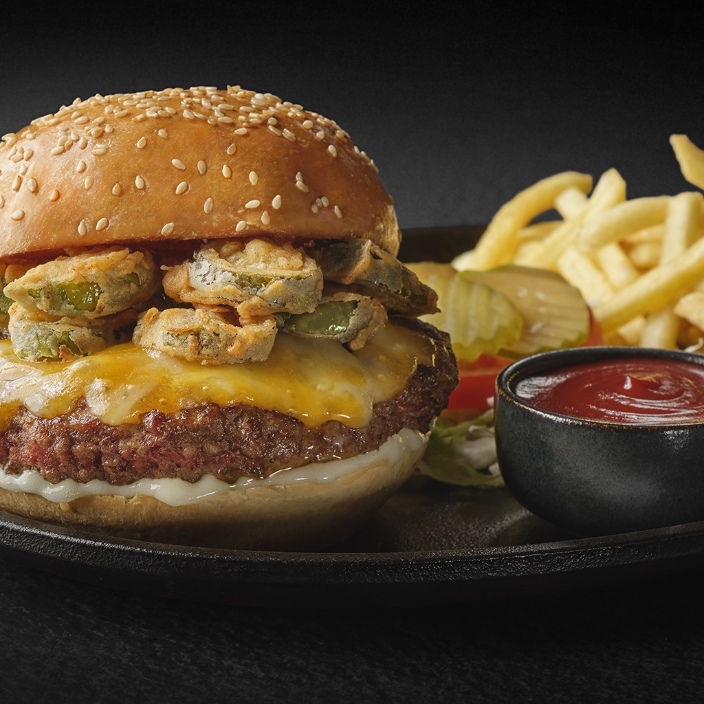 A juicy burger topped with fried jalapeños and melted cheese, served with fries and ketchup.