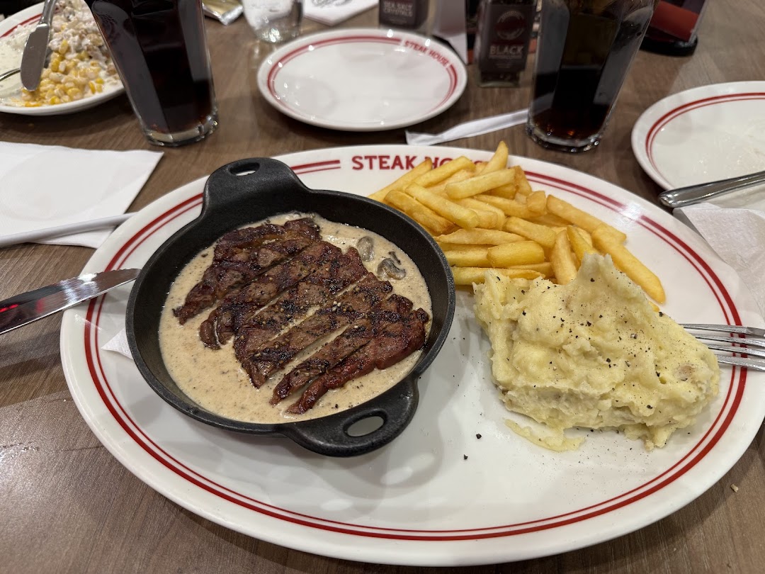 A sliced steak with creamy sauce, french fries, and mashed potatoes on a plate.